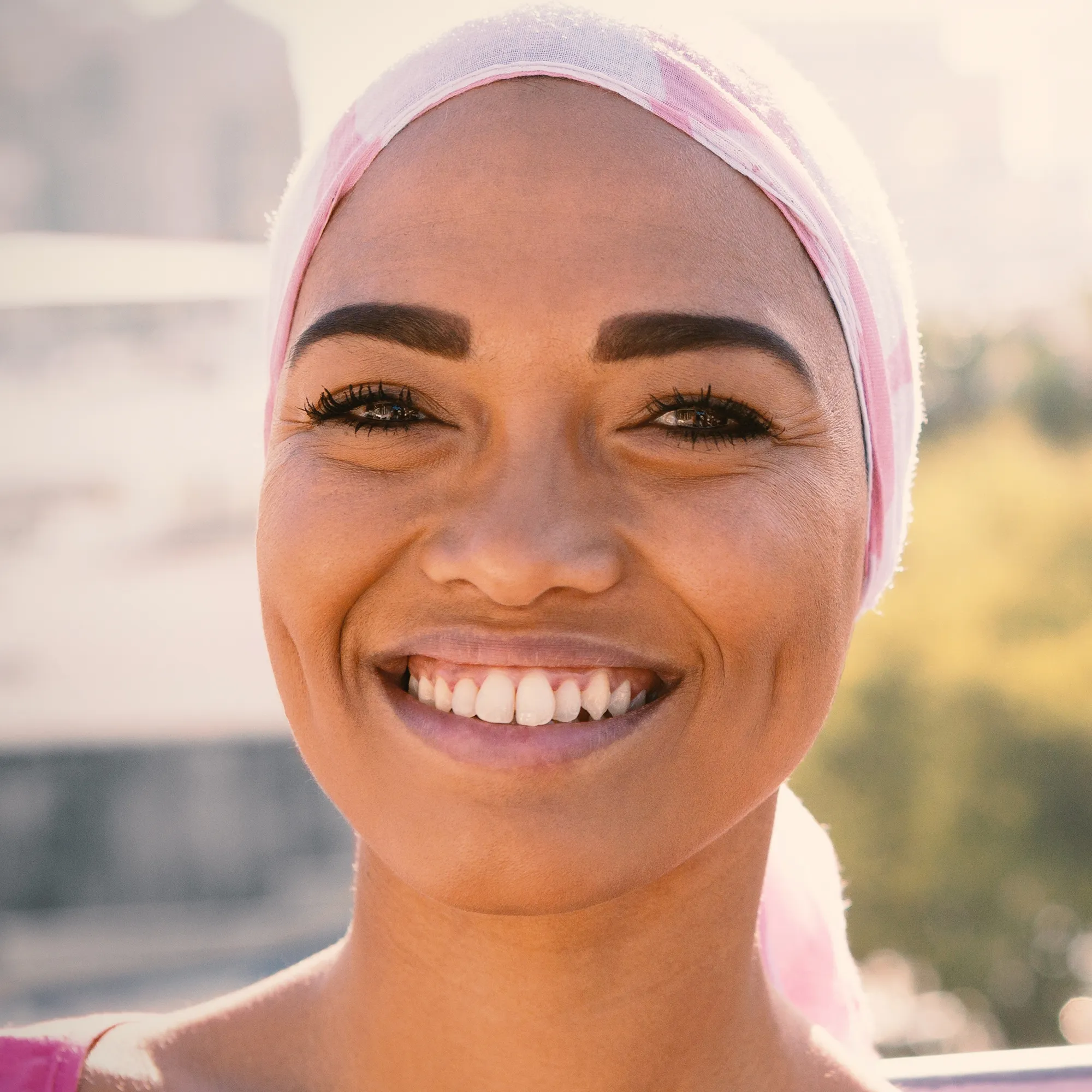 Grace Thomas smiling outdoors, wearing a pink head wrap